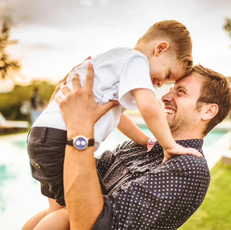 A smiling father lifts his young son in the air, symbolizing a successful reunification after therapy. A heartwarming moment of trust, healing, and connection.