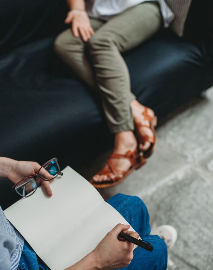 Close-up of a mental health therapy session, featuring a client with a notebook and a therapist listening actively.
